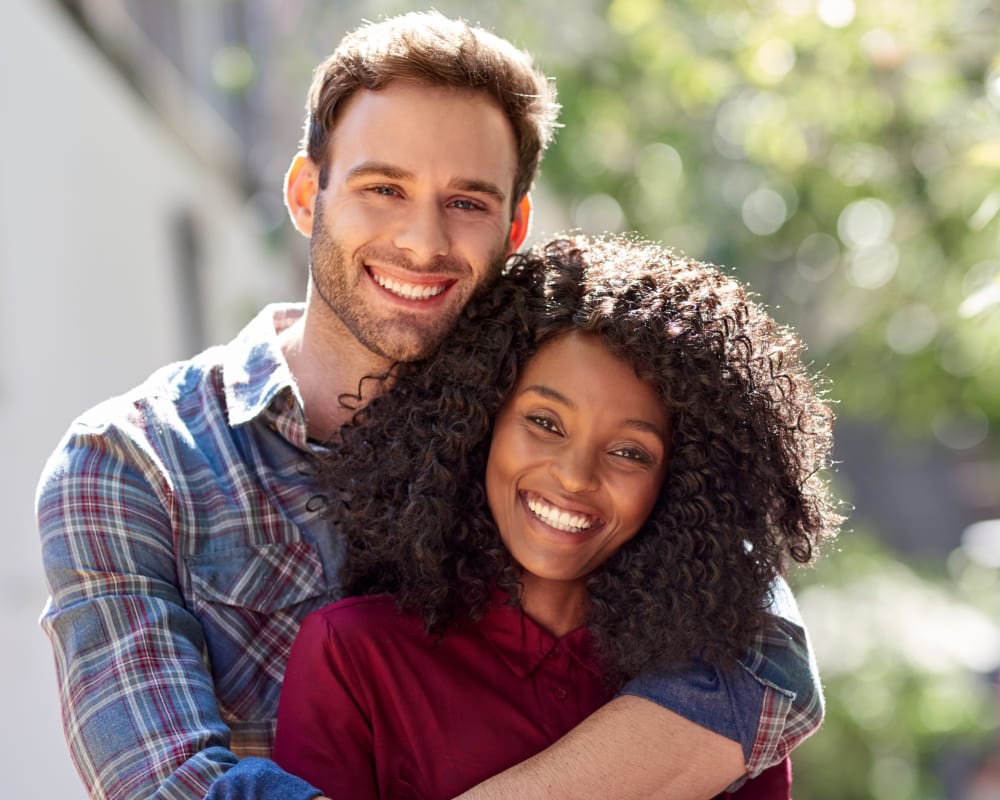 A man and a woman embrace as they smile at the camera.