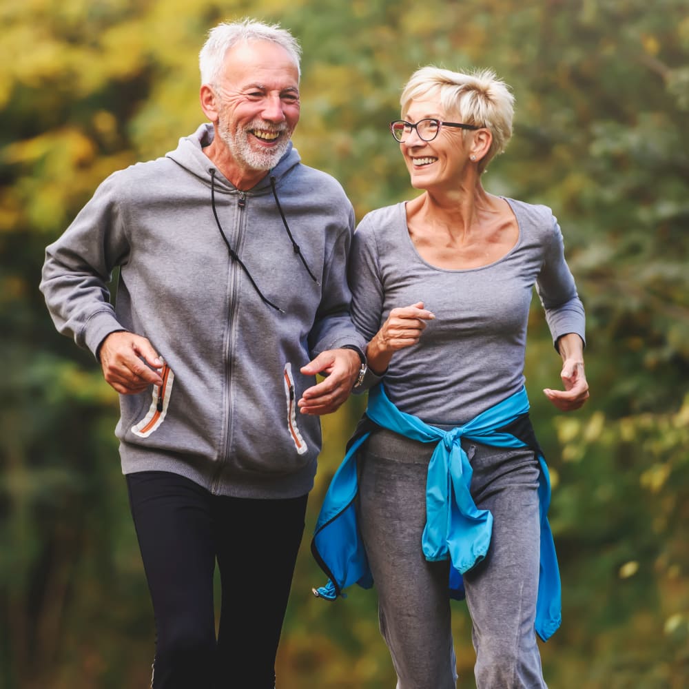 An older couple are jogging on a trail and laughing.