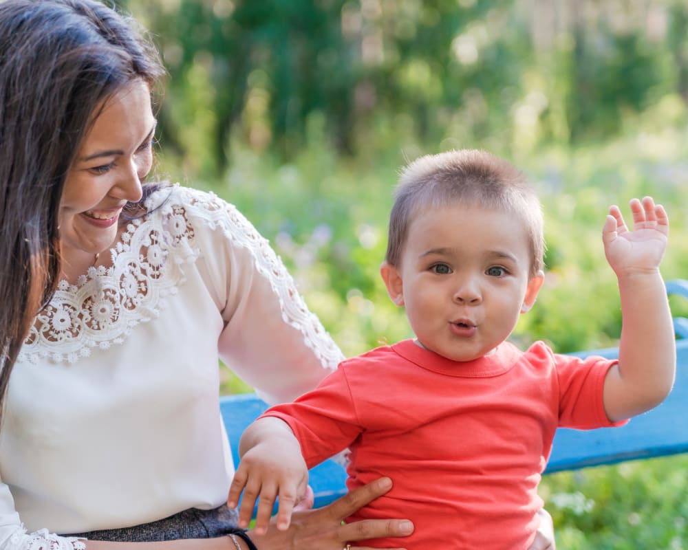 A mom smiles at her toddler, who is making a silly face and doing a dance.