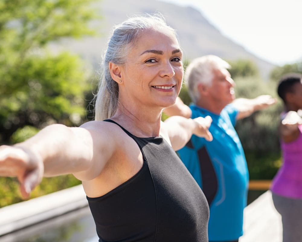 An older woman is doing group yoga outside.