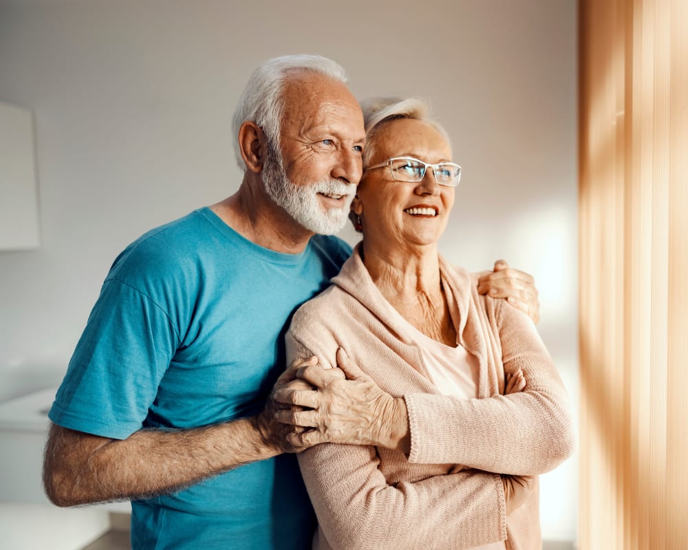 An older man and woman are holding hands while looking out a window.