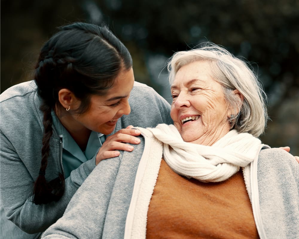 A young woman and an older woman laughing together in a park.
