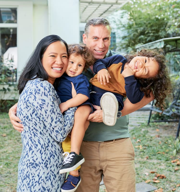 A family of four smiles at the camera. Each parent is holding a young boy, and the boy the dad is holding is making a silly face.