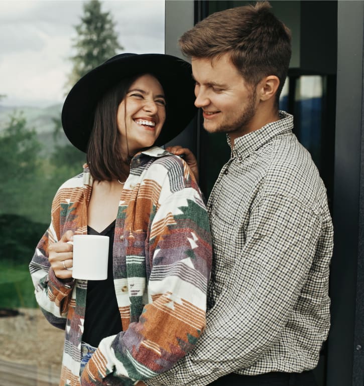 A young adult man and woman hug while standing outside.